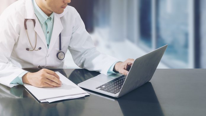 Doctor,Working,With,Laptop,Computer,And,Writing,On,Paperwork.,Hospital,AI,in,Healthcare